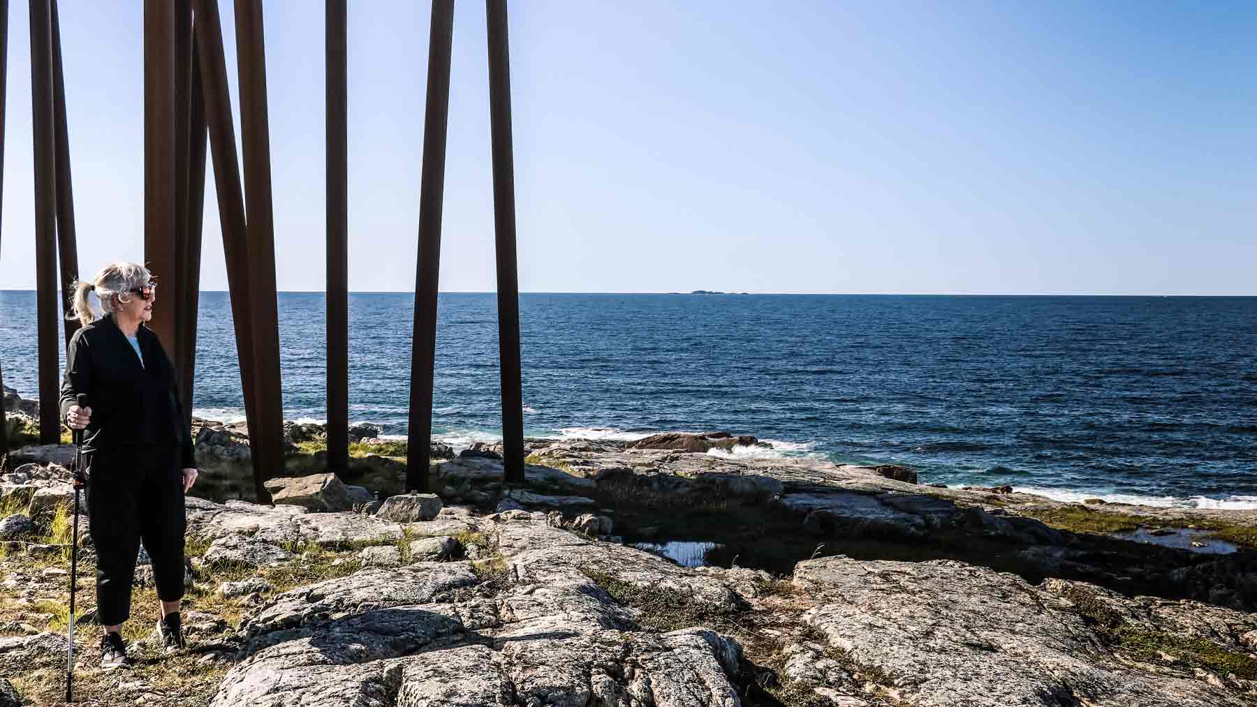 The Asmuss founder's Mum wearing Asmuss Pleated Zip Through Sweat and Asmuss Panelled Trousers in front of the supporting beams under the Fogo Island Inn
