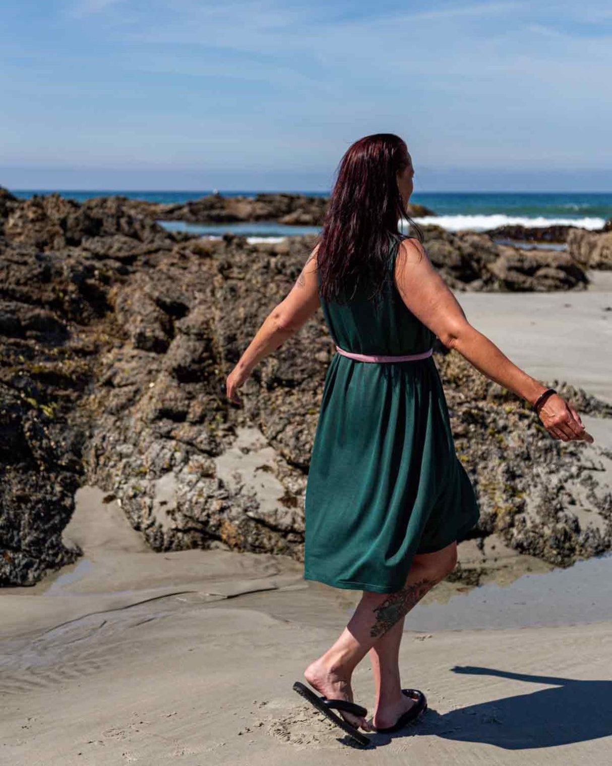 Woman spinning around at a beach wearing the Asmuss Drift Dress with the pink waist tie cinching in the dress