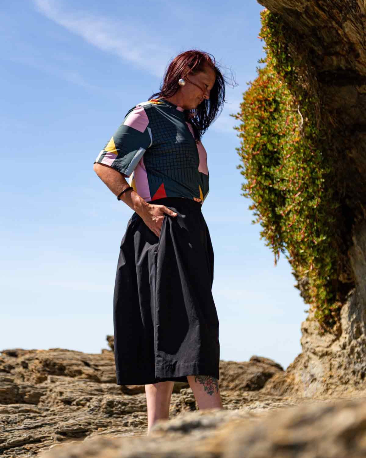 Woman standing on rocks wearing the black Kate Culottes and geometric patterned Drew T-shirt. Her hand is in one of the pockets