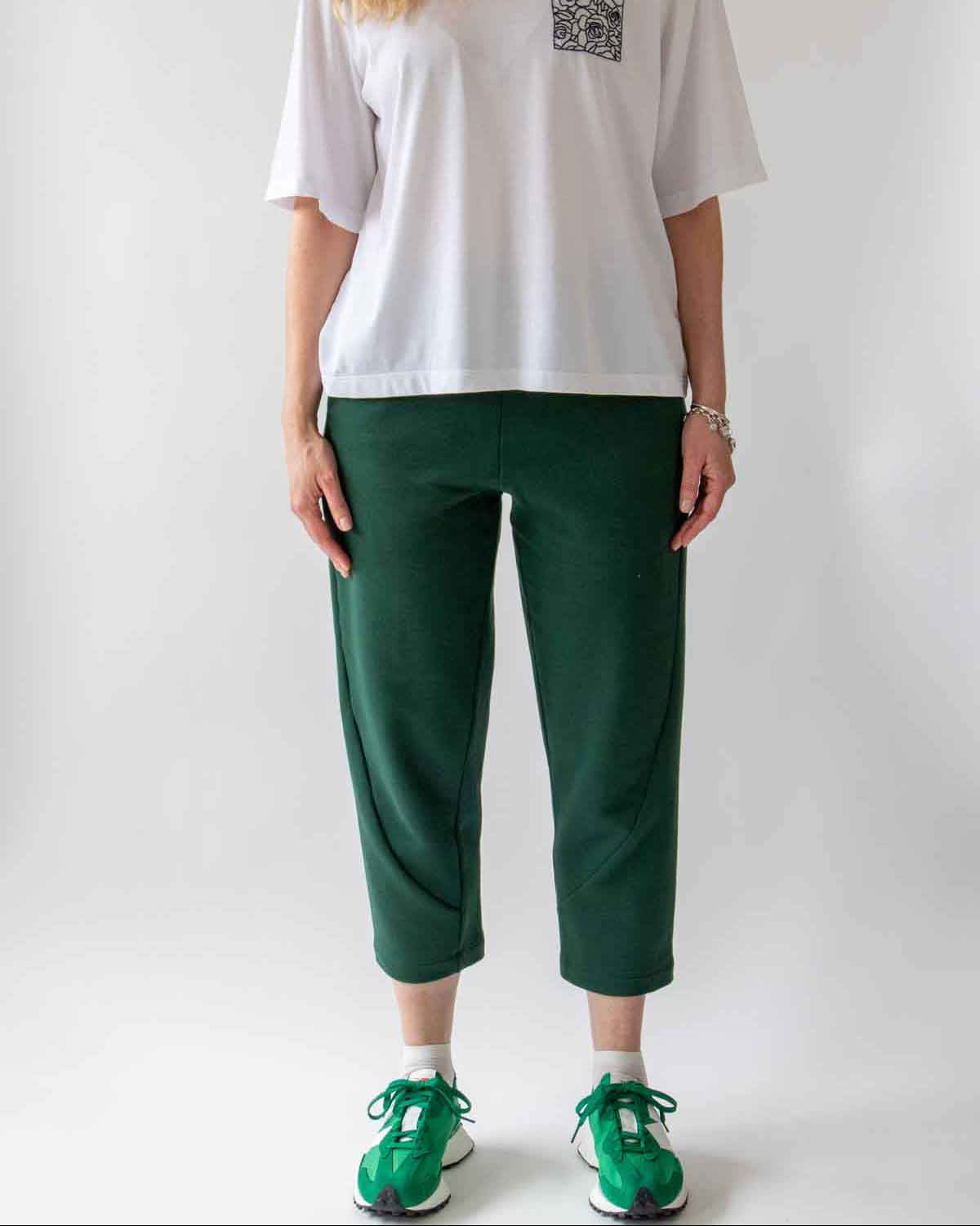 Woman standing front on wearing the Asmuss Curve Joggers in Trekking Green and Evelyn Tshirt in White with Black Rose Embroidery and bright green trainers