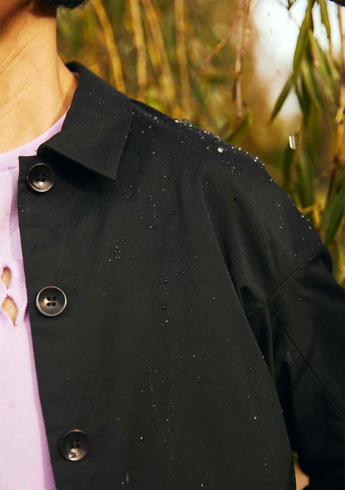 Close up of the left shoulder of a woman wearing the Asmuss Roam Jacket showing water beading on the Bio Castor Bean fabric, showing the water resistance of the fabric