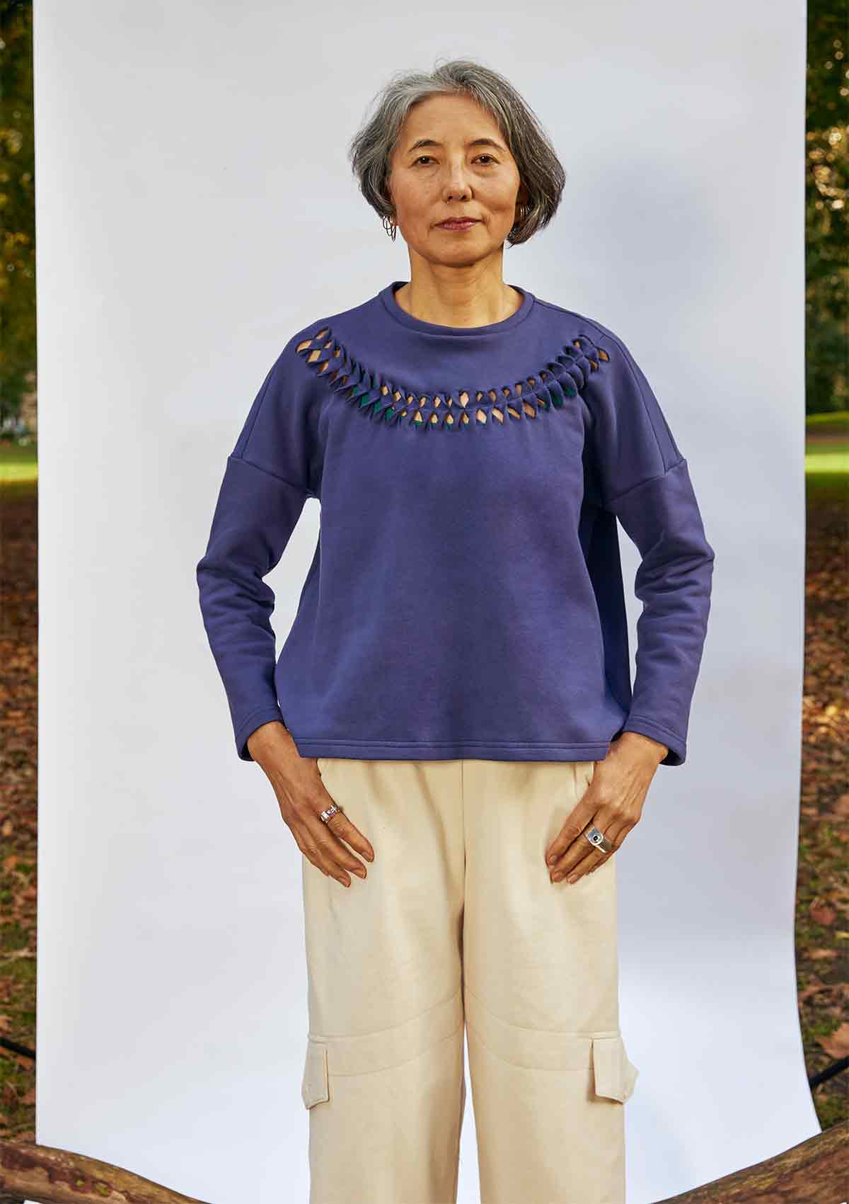 Women standing face on wearing the Anni Sweatshirt in Navy with detailing where the fabric is cut, twisted and stitched back in place.  She is standing in front of a white background in a park