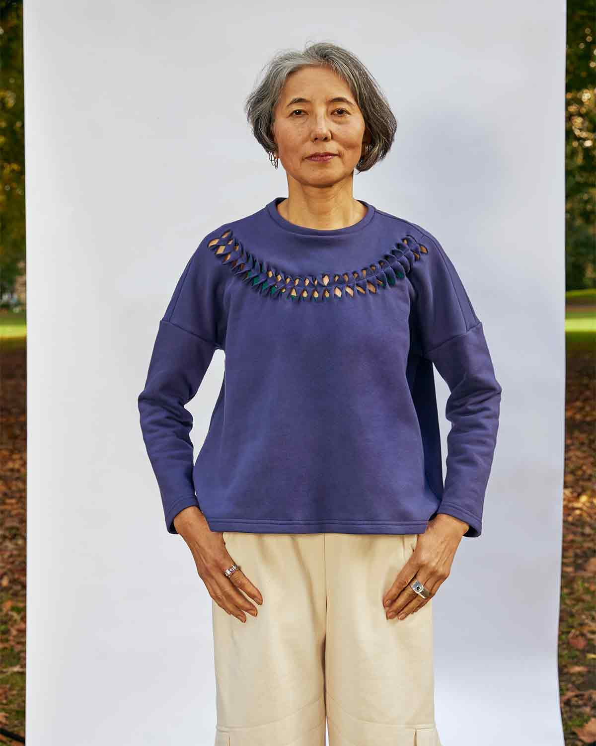 Women standing face on wearing the Anni Sweatshirt in Navy with detailing where the fabric is cut, twisted and stitched back in place.  She is standing in front of a white background in a park