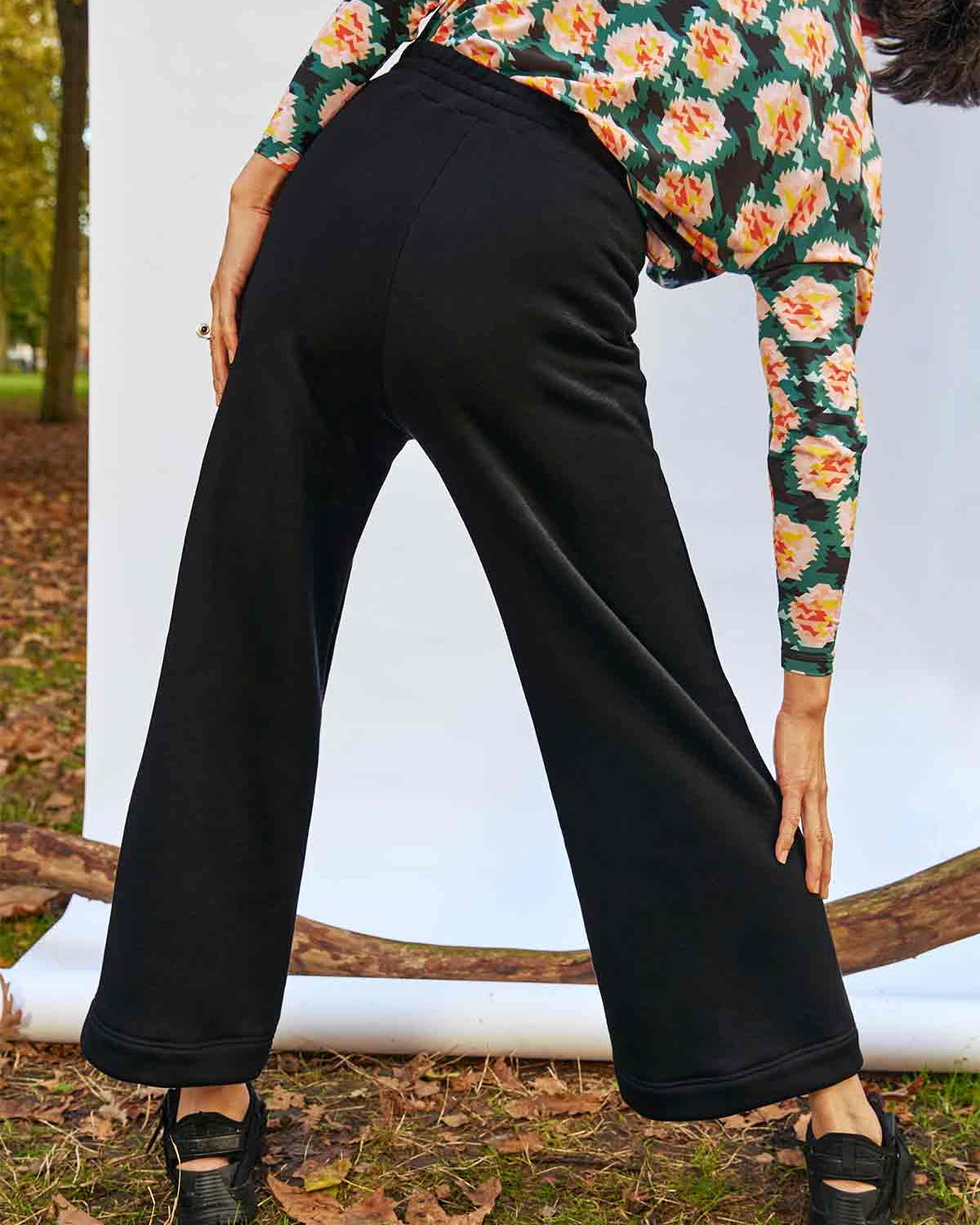 Woman standing, with a wide stance,  facing away bending to the right with a her hand on her calf.  She is wearing the Asmuss Column Joggers
