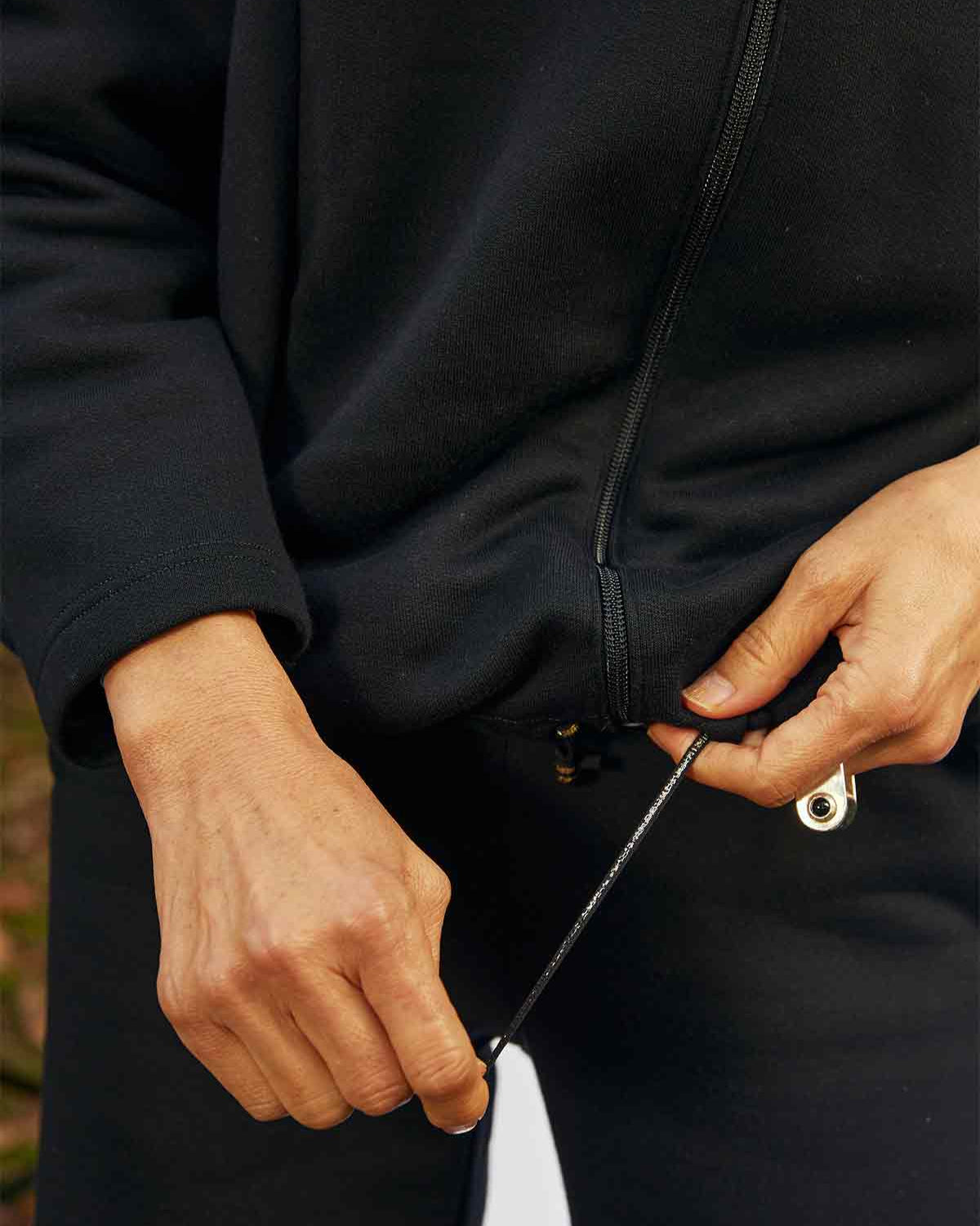 Close up of a woman tightening the hem of the Asmuss Hepworth Zip Through Sweatshirt.  The drawa string is black with a gold stripe