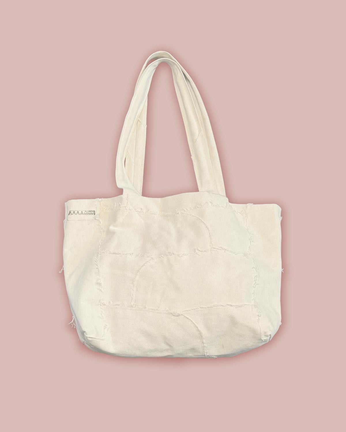 Flat front view of the Asmuss Scraps Tote bag, showing the stamped Asmuss logo and the raw edges of the panelled together bag.