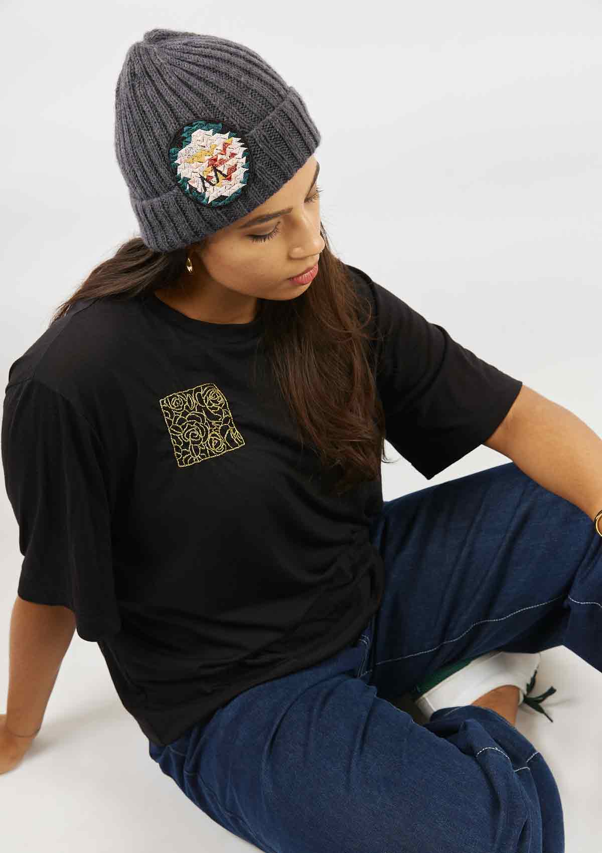 Woman sitting on the floor wearing the Asmuss hand knitted, hand dyed beanie in Almost Black and the Asmuss Evelyn tshirt black