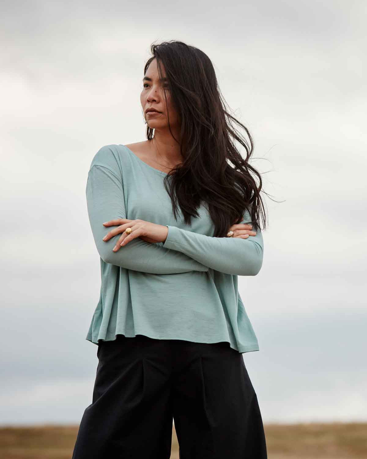 A modern woman standing strong in the beautifully falling Asmuss Long Sleeve A-line T-shirt in Sea Green. An elevated for all your everyday adventures it is made from soft wool blended with 37.5 Technology to help regulate your body temperature