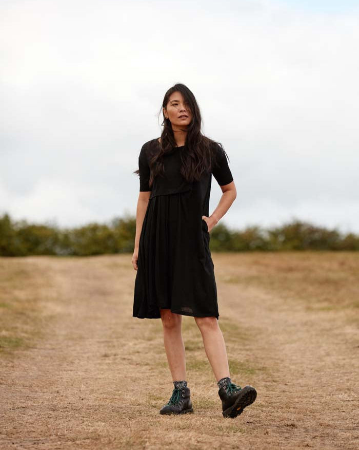 Woman wearing the Asmuss Asymmetric Pleat Dress in Black. A little black dress that can take you from the office, to gallery, restaurant or any other everyday adventure.