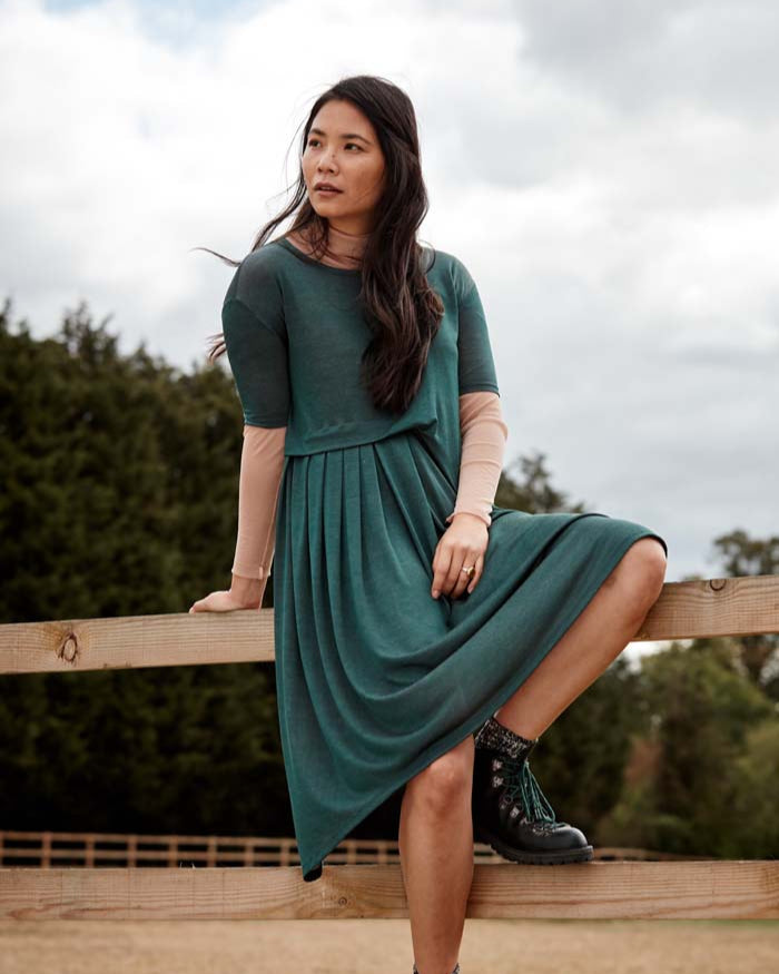 Woman wearing the Asmuss Asymmetric Pleat Dress in Pine Green. Slim arms, loose fitting body with pleat detail and pocket it makes a great dress for your everyday adventures. Made from a blend of recycled polyester and Tencel a great sustainable fabric. A stylish, sustainable addition to the modern woman's wardrobe.