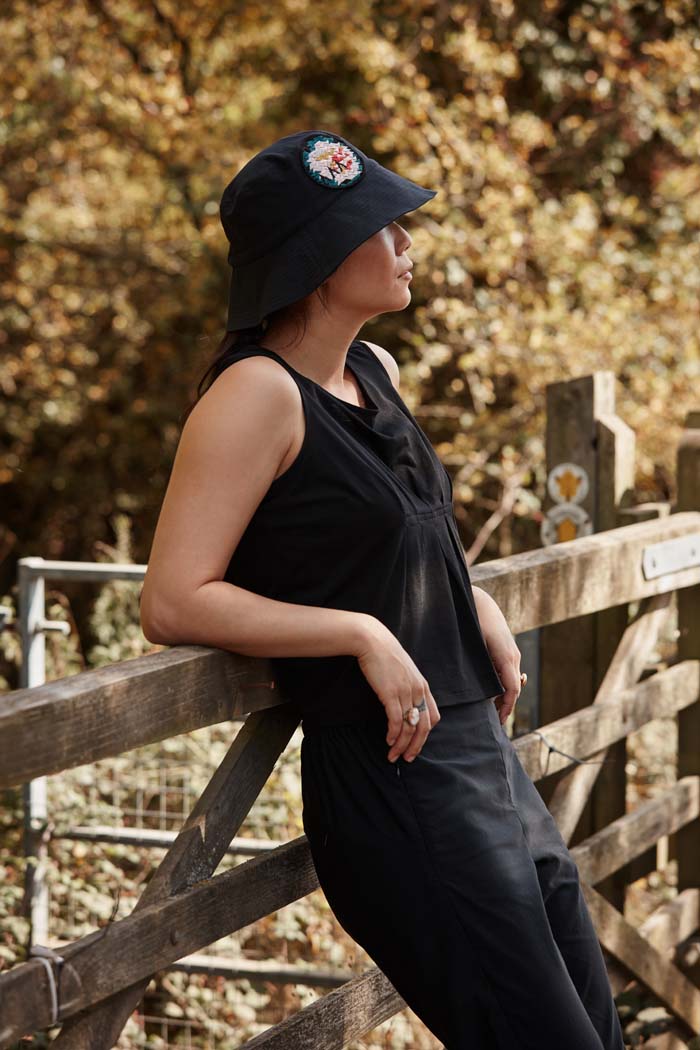 Woman leading on her elbows relaxing during a walk in the countryside wearing the Asmuss Wide Brim Bucket Hat in black with rose embroidery badge. The perfect sun hat to keep the sun off your face but still look good and with water resistance to keep the rain off too.