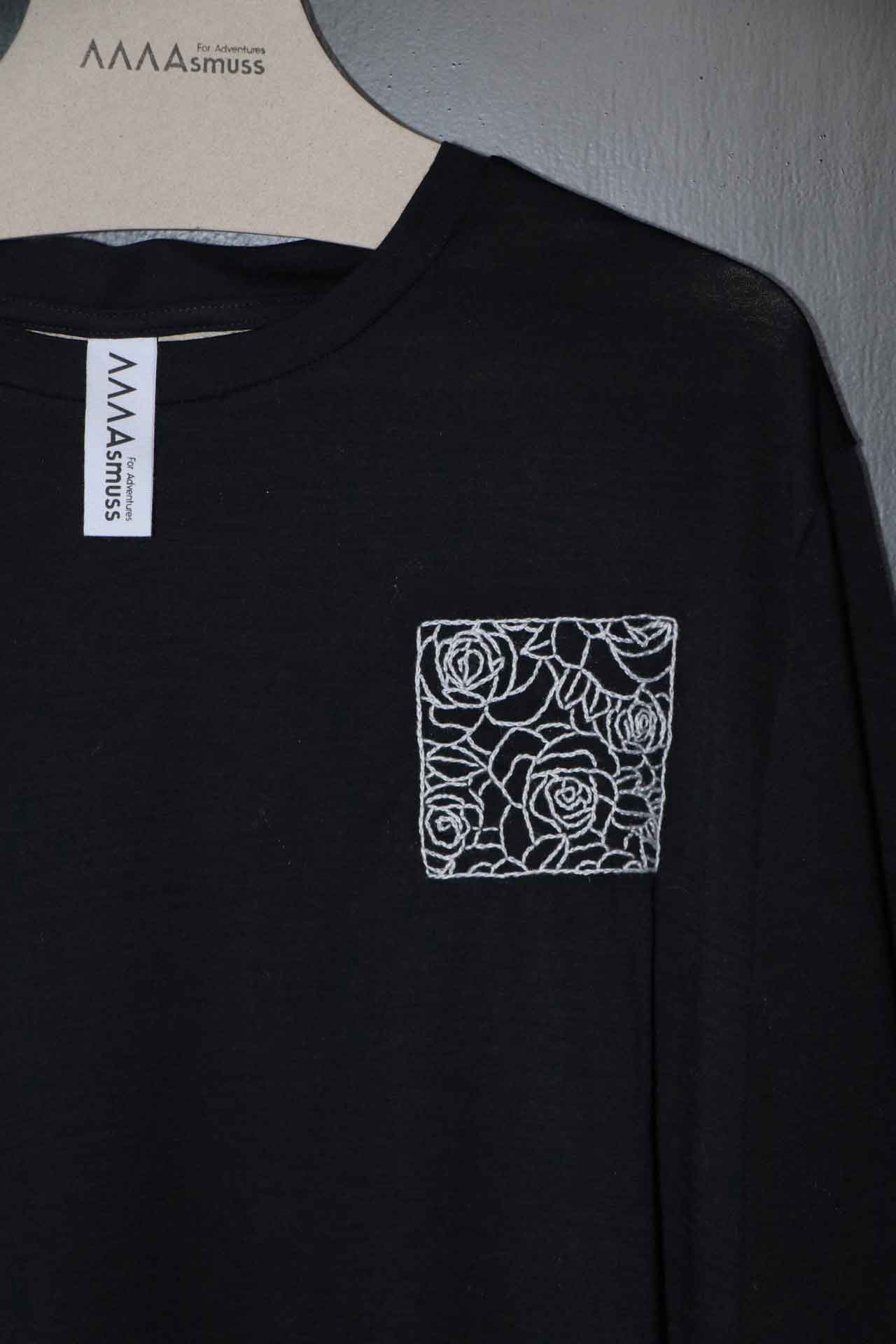 Close up of hand embroidery on black Evelyn Tee. The embroidery is white outline of roses in a square