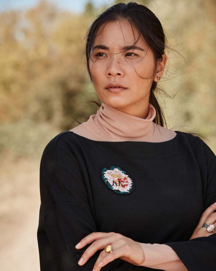 Woman wearing the Asmuss Oversized Boat Neck Sweat in black with embroidered rose badge. Stylish, sustainable lifestyle womenswear for any of your everyday adventures whether they are everyday or when you are travelling