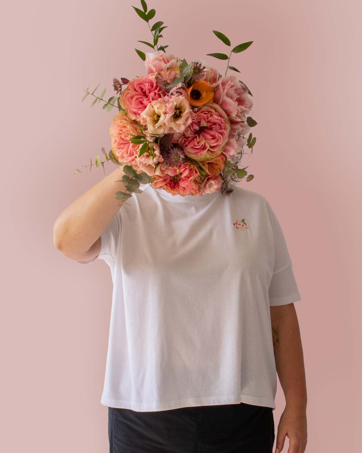 Asmuss Boxy T-shirt in White Organic Cotton and Recycled Polyester with Embroidered Rose detail worn by Clare holding a beautiful bunch of flowers, that echo the embroidery, in front of her face.