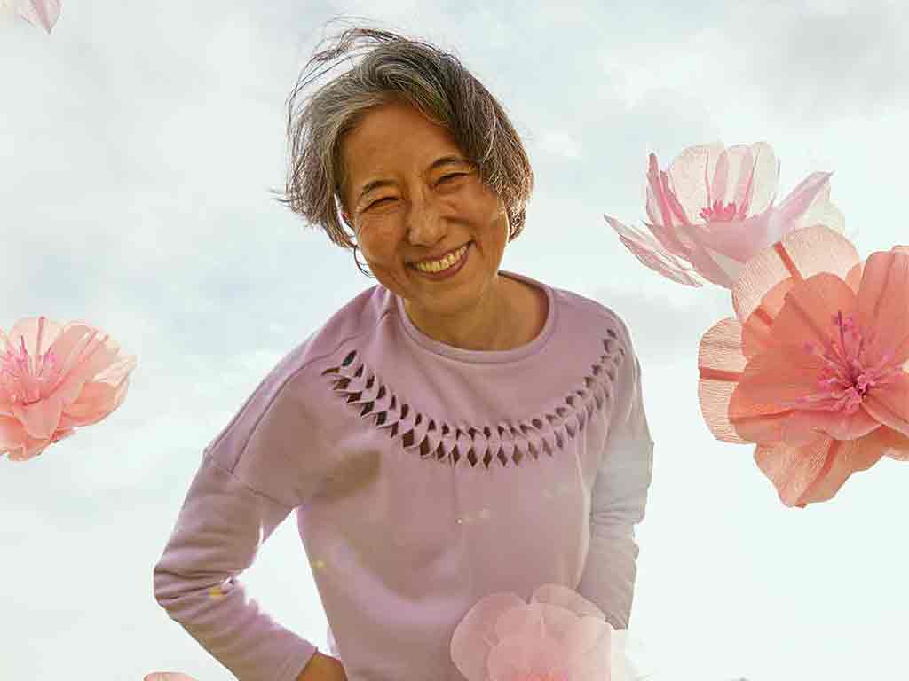 Woman leaning forward smiling wearing the lilac Anni Sweatshirt with large pink flowers floating around her