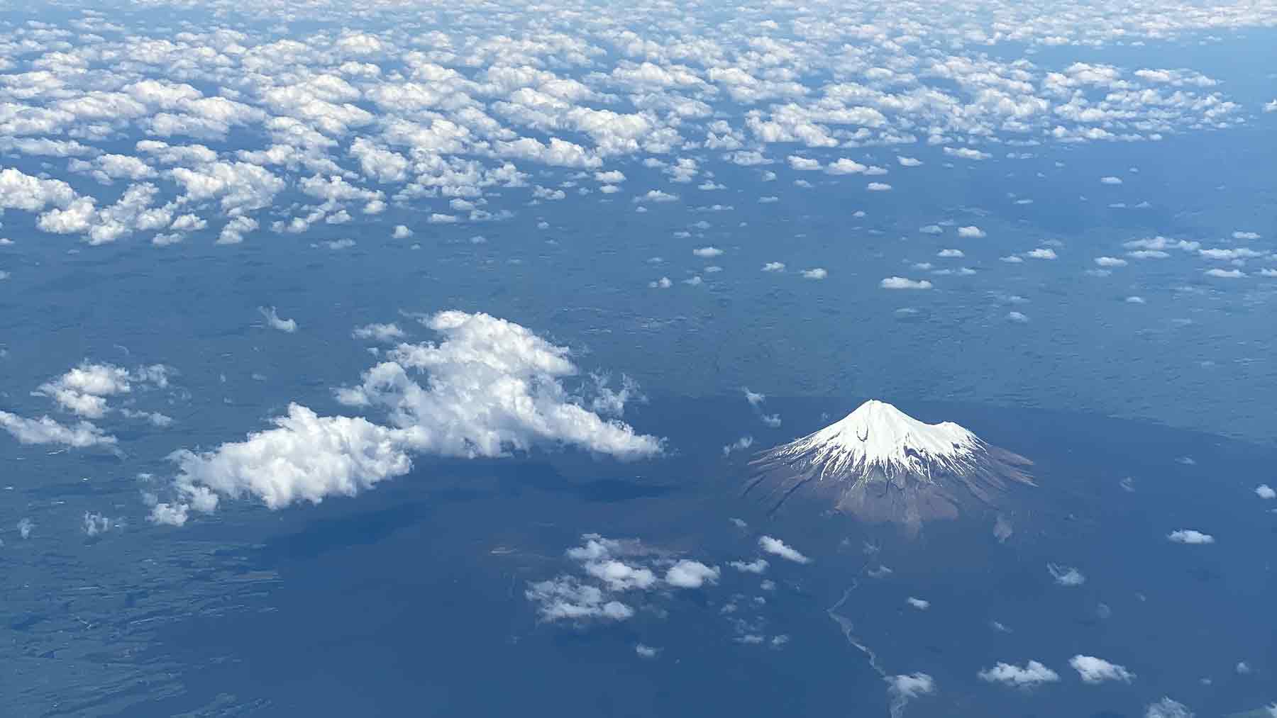 Snow covered Mount Taranaki and the coast of Taranaki from an airplane with little fluffy white clouds