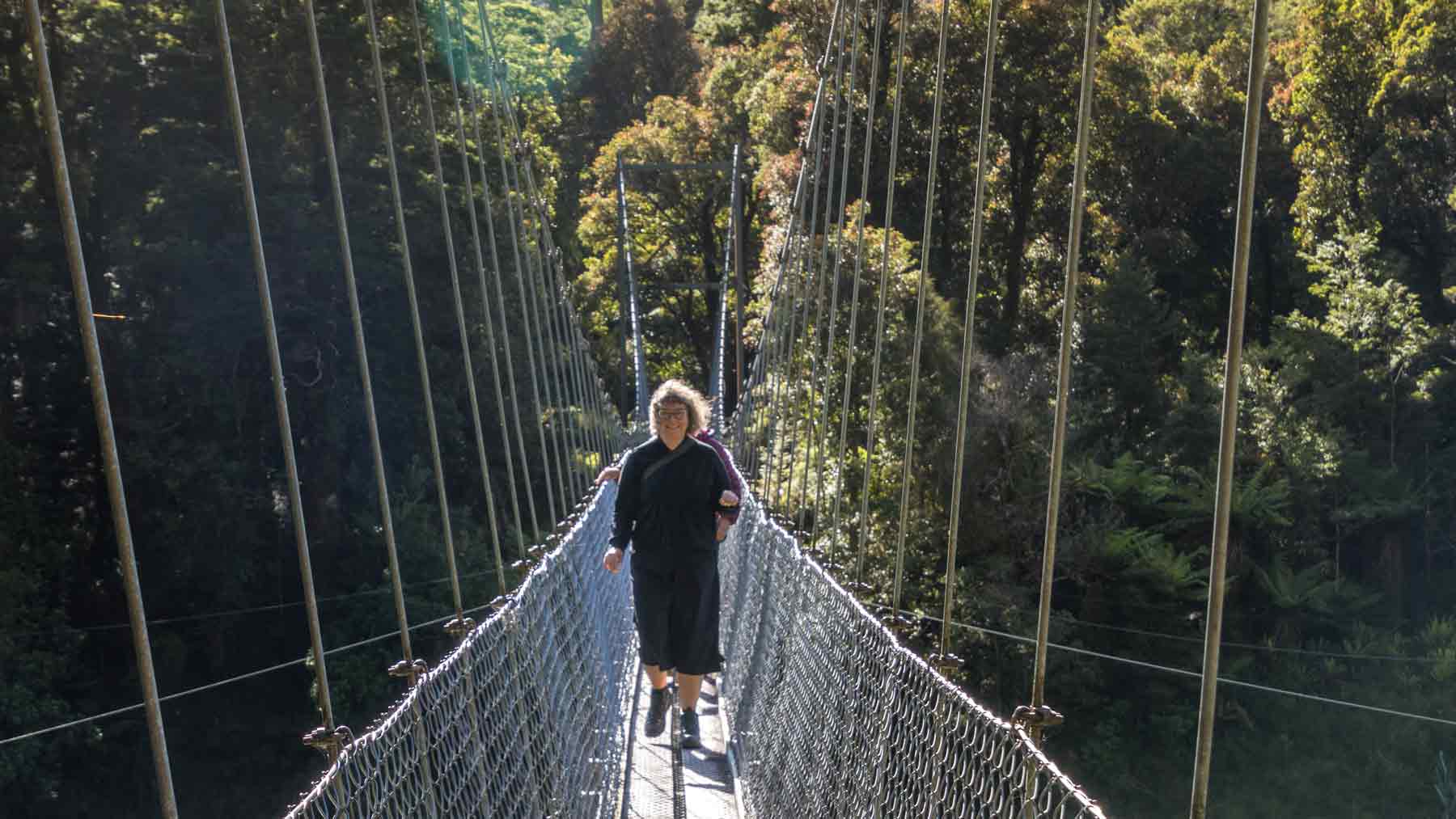 Crossing a swing bridge on the Hollyford Track wearing Asmuss