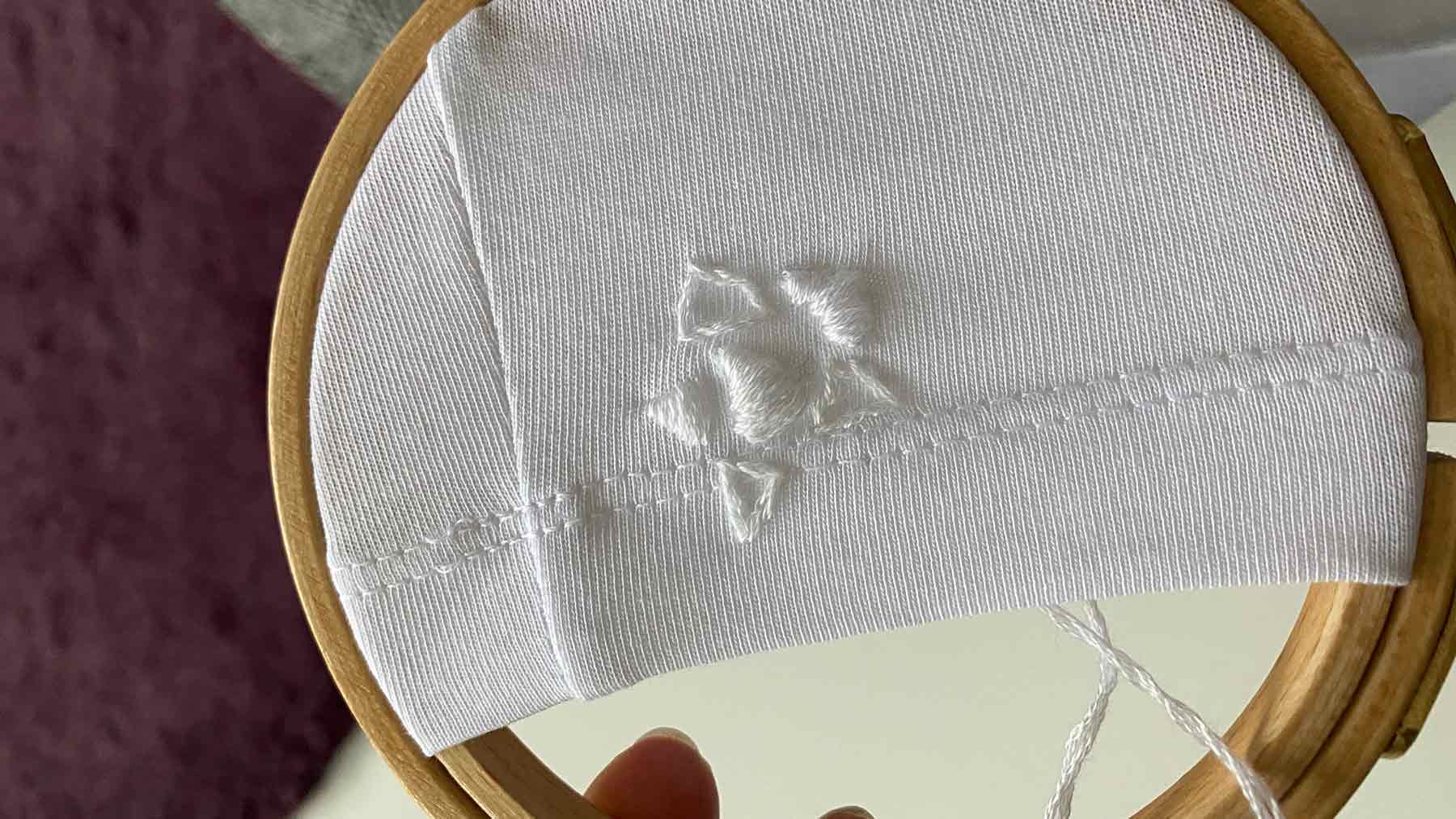 White geometric rose embroidery being embroidered onto a white t-shirt to mend a hole
