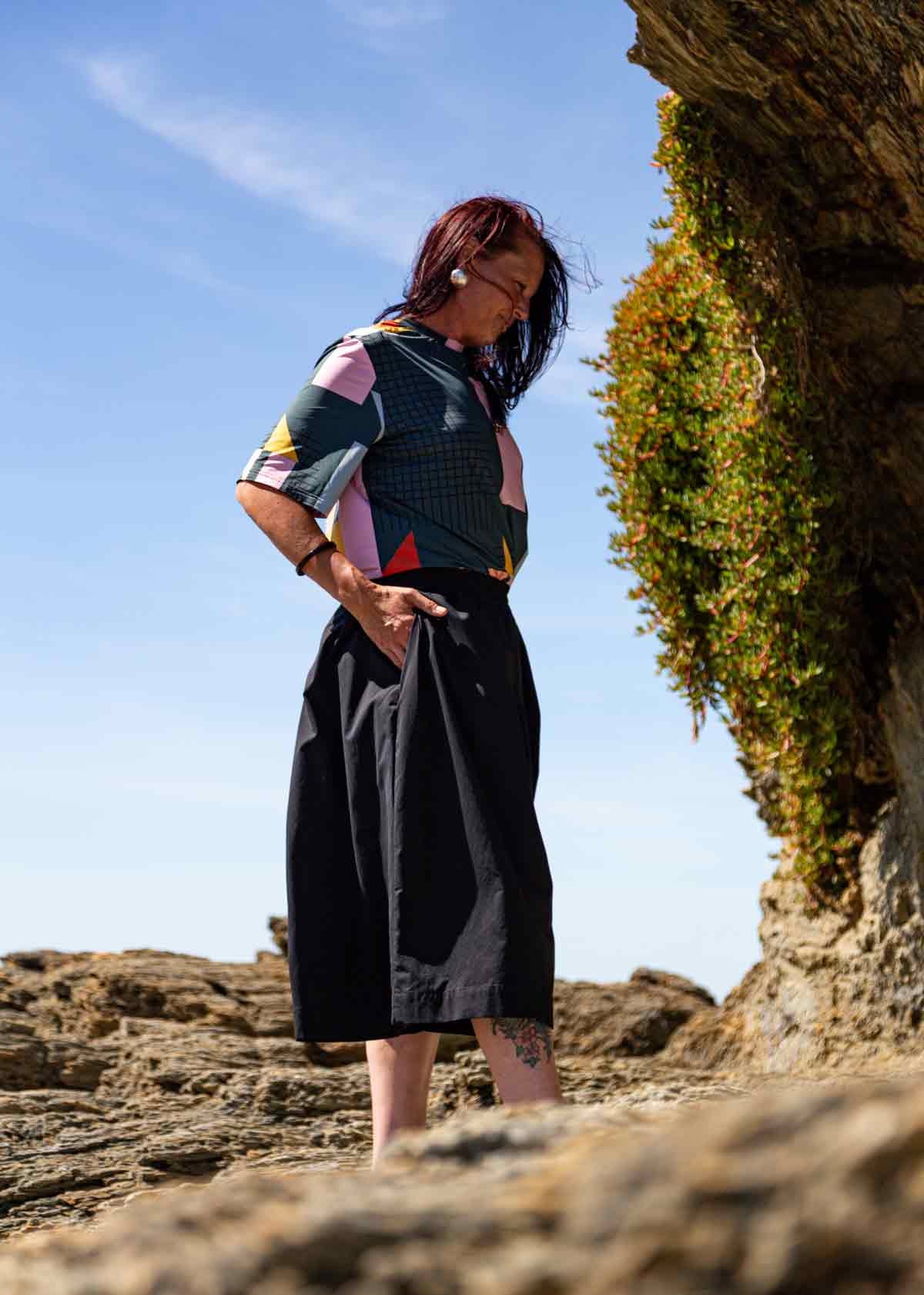 Woman standing on rocks wearing the black Kate Culottes and geometric patterned Drew T-shirt. Her hand is in one of the pockets
