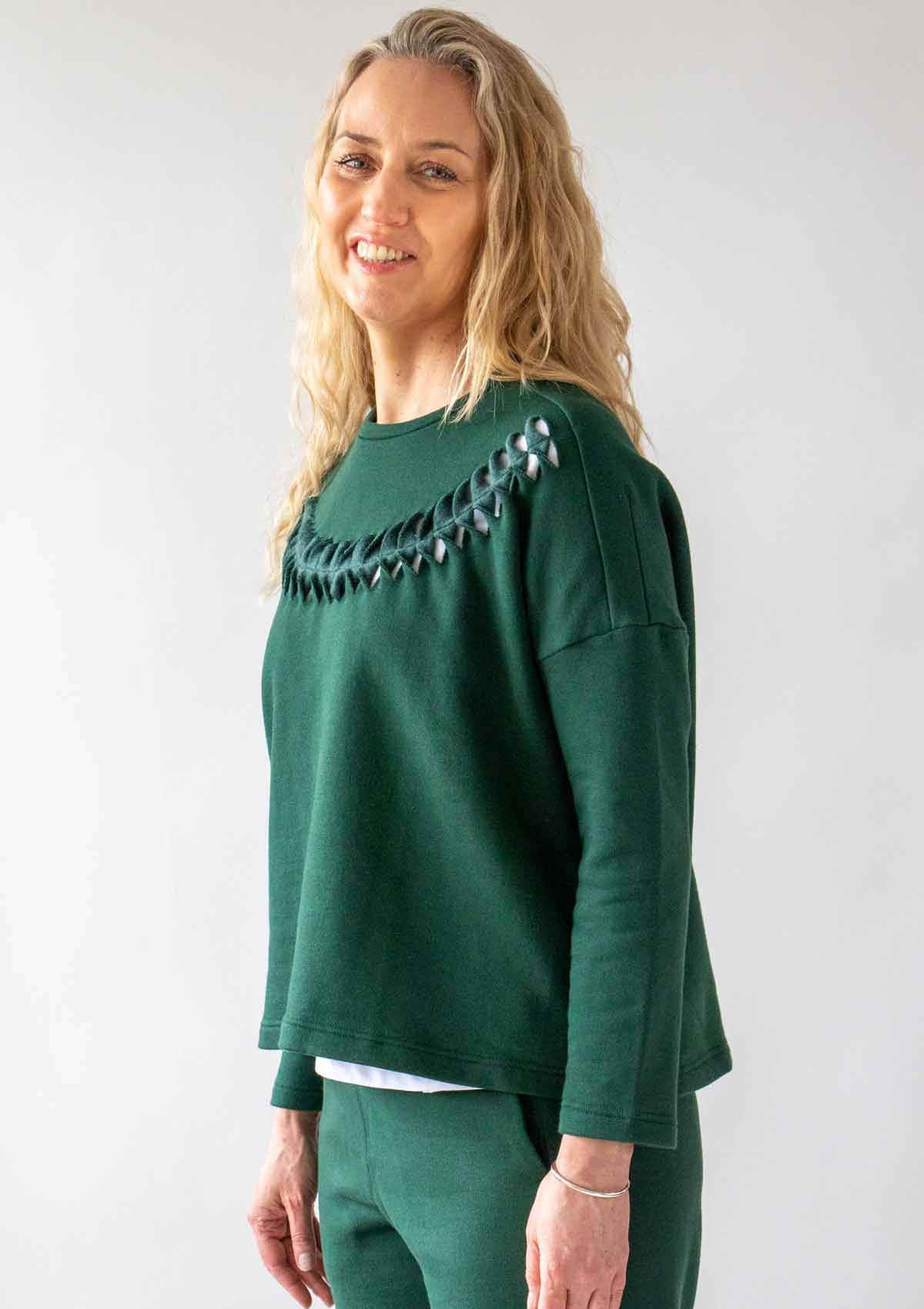 4.	Woman smiling, with long wavy blond hair, wearing the Asmuss Anni Sweatshirt with the Cut Twist and Stitch detailing