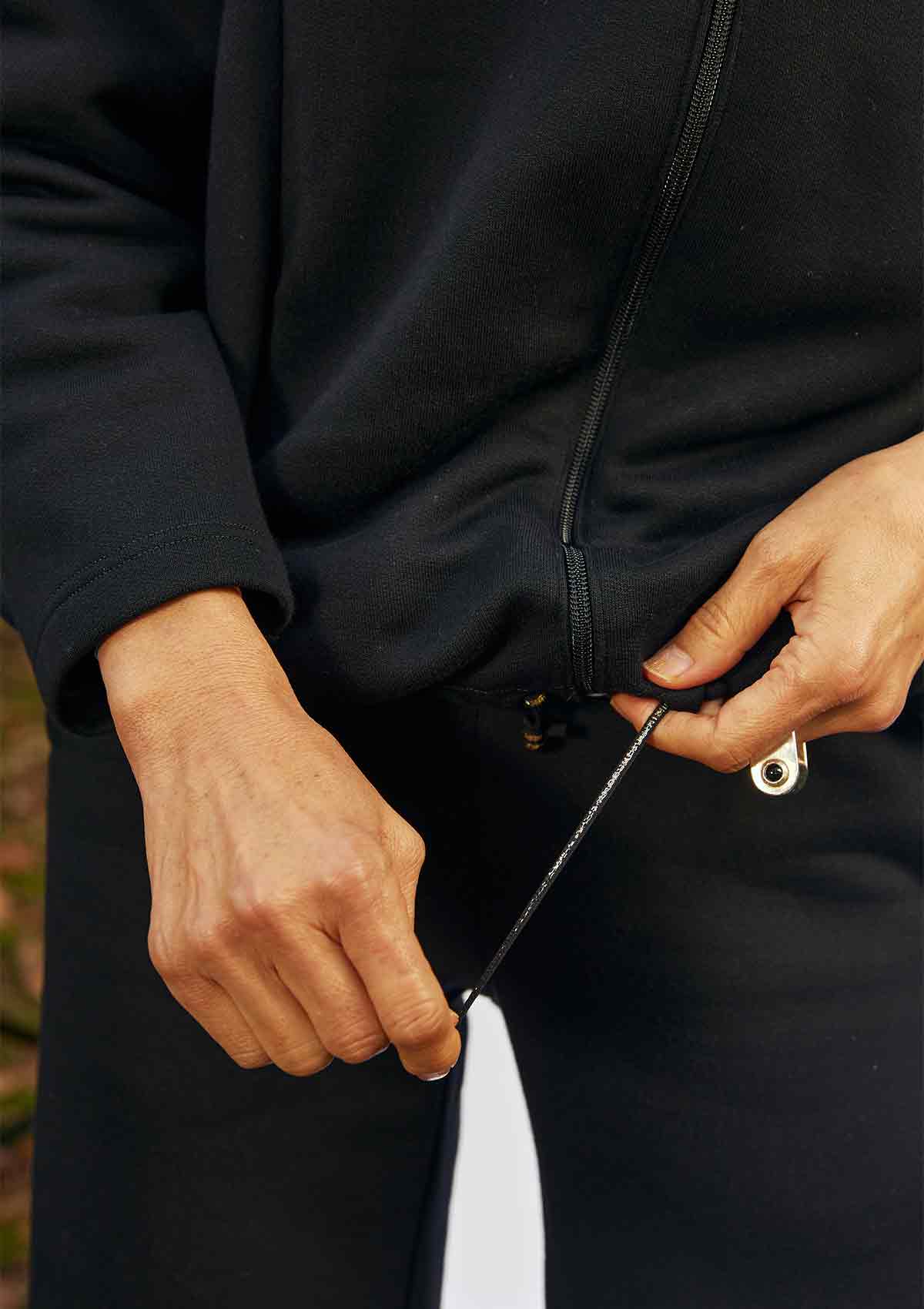 Close up of a woman tightening the hem of the Asmuss Hepworth Zip Through Sweatshirt.  The drawa string is black with a gold stripe