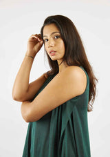 Dark haired woman standing sideways to show inverted pleat detail in the pine green Asmuss Drift Dress.  The dress is sleeveless