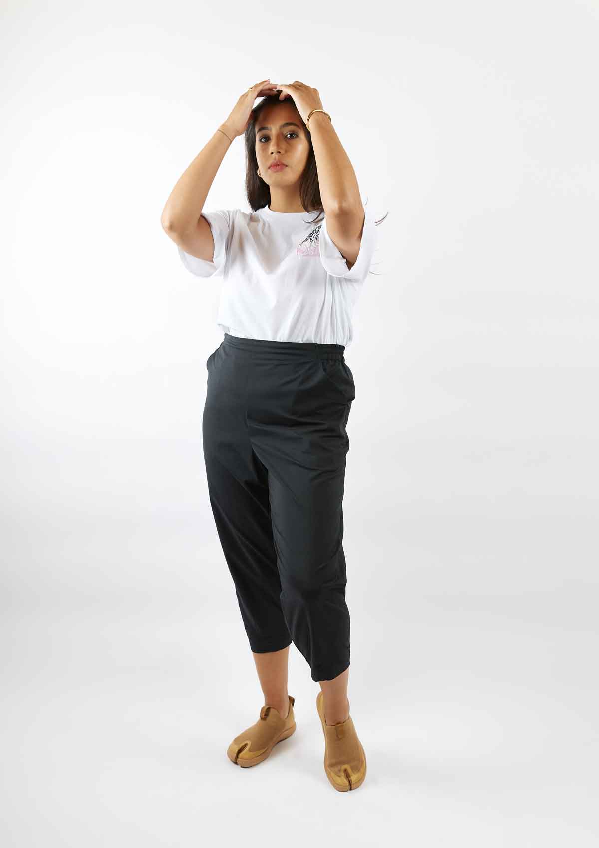 Woman standing with her hands on her head wearing the Asmuss Evelyn tshirt in white with black and pink rose square hand embroidery and the Asmuss Oval Trousers in Black
