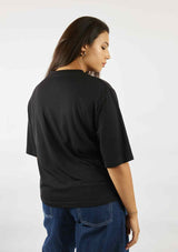 Woman standing with her back to us wearing the black Asmuss Evelyn Tshirt untucked