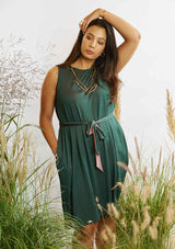 Woman with a hand over her head and the other in the pocket of the Asmuss Drift Dress that is belted with the self fabric belt while standing amongst grasses