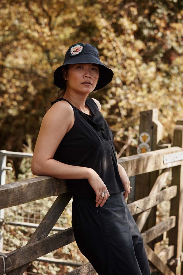Woman leading on her elbows relaxing during a walk in the countryside wearing the Asmuss Wide Brim Bucket Hat in black with rose embroidery badge. Made from water resistant sustainable fabric it is the perfect sun hat to keep the sun off your face but still look good and keep the rain off too.