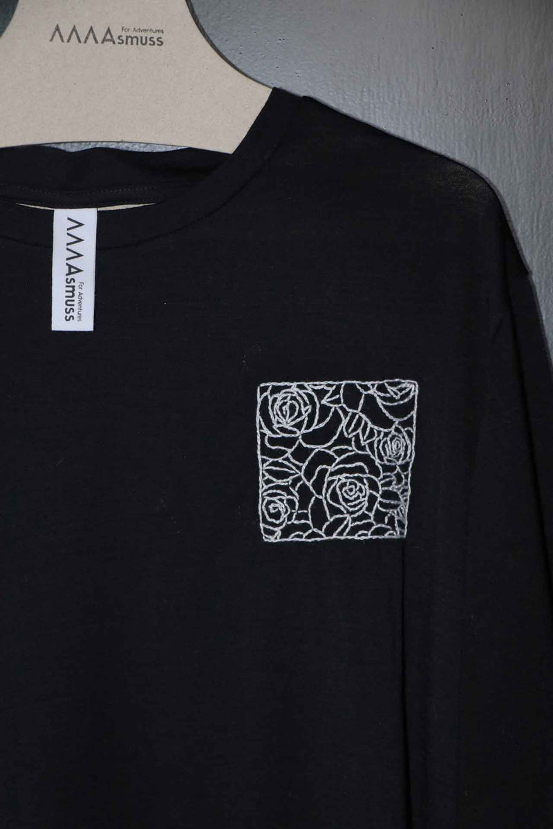 Close up of hand embroidery on black Evelyn Tee. The embroidery is white outline of roses in a square