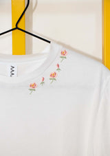 Close up of white Evelyn tee-shirt with hand embroidered small geometric roses and rose buds in pinks and green, placed following the neckline on left hand side of the tee-shirt  